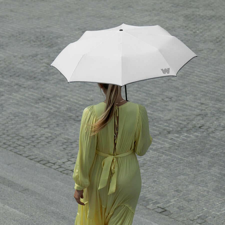Woman walking down stairs while holding an opened Weatherman Travel Umbrella in white.