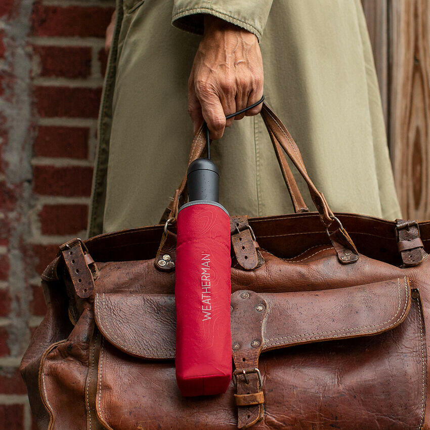 Person walking with closed Weatherman Travel Umbrella in red in their hand.