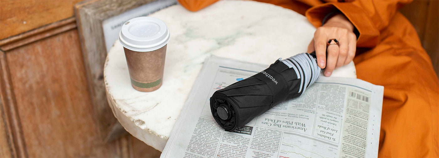 A man with a folded umbrella is reading a newspaper.