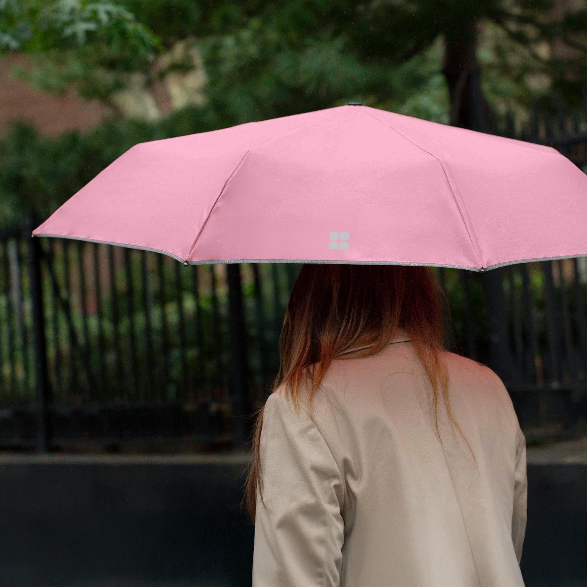 Woman walking down the street while holding an opened Weatherman Travel Umbrella in blush.