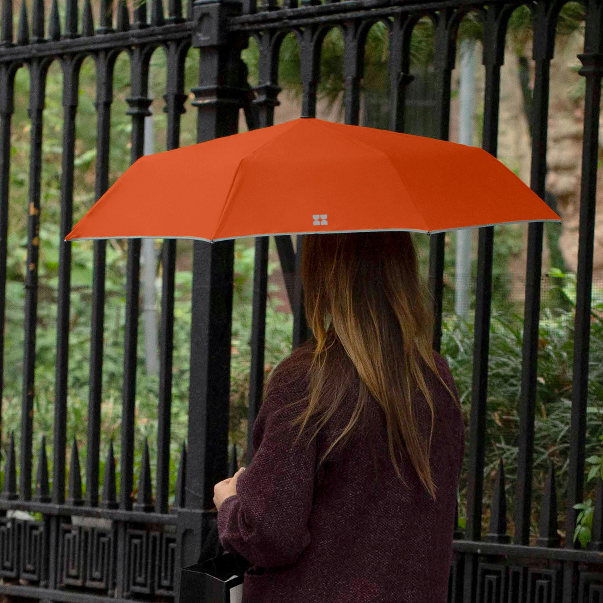Woman walking down the street while holding an opened Weatherman Travel Umbrella in rusty orange.