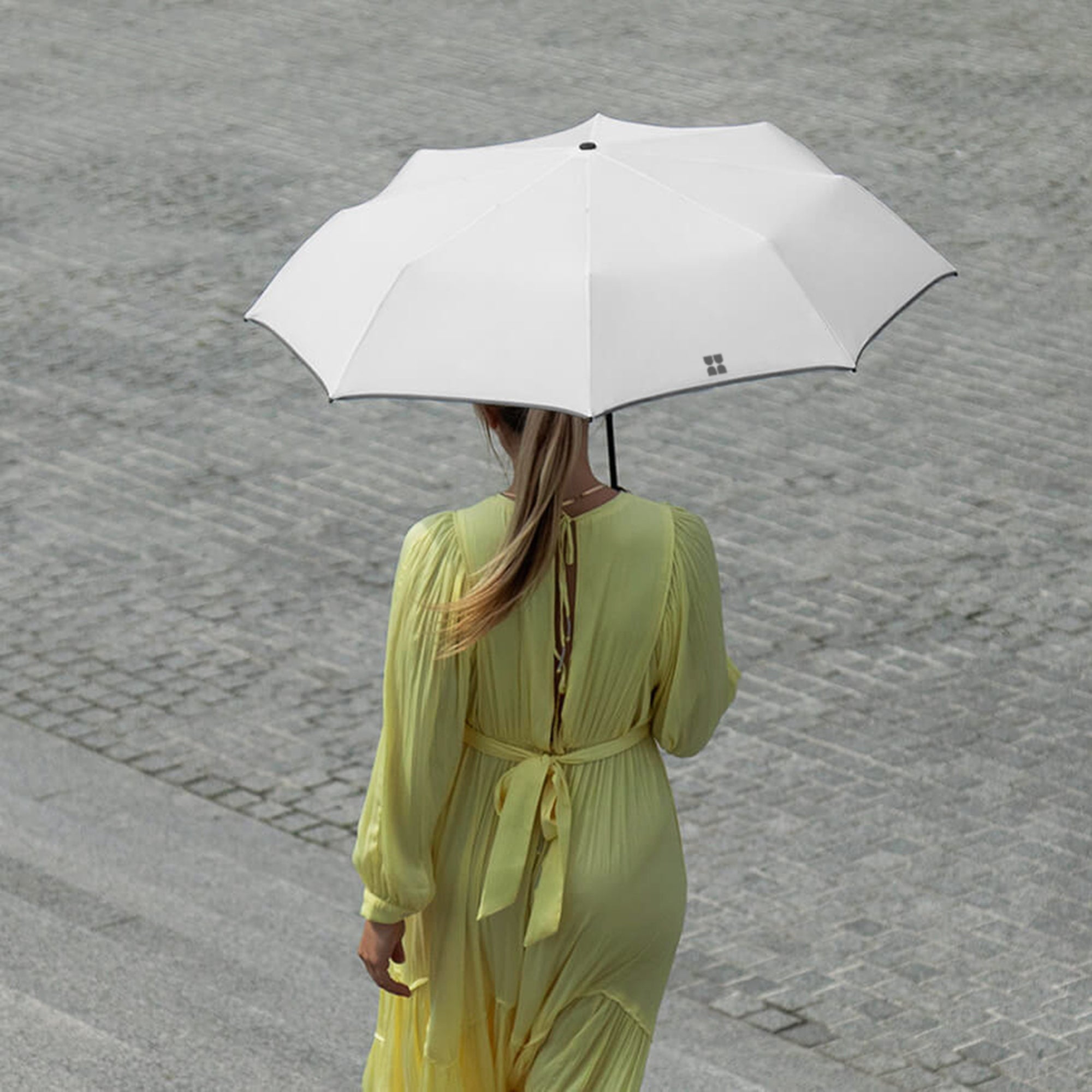 Woman walking down stairs while holding an opened Weatherman Travel Umbrella in white.