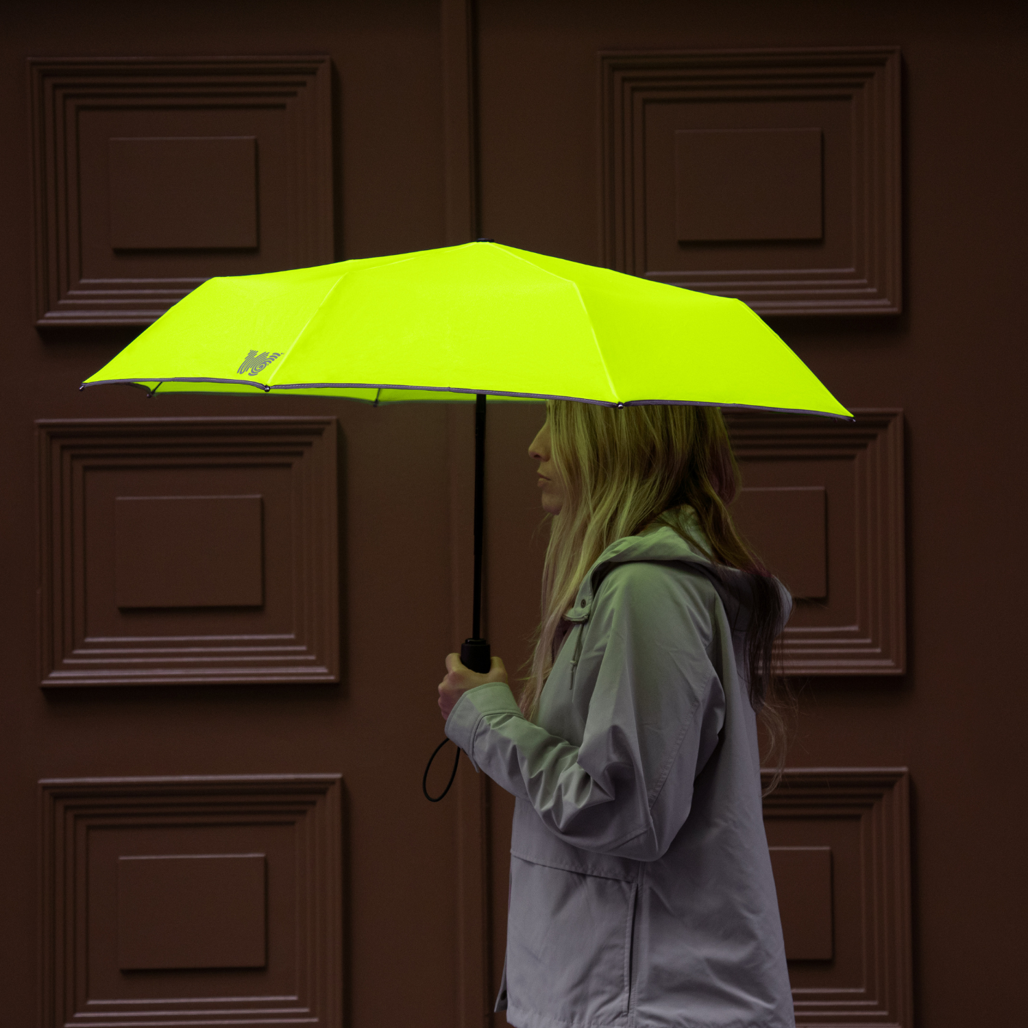 Woman walking with opened Weatherman Travel Umbrella in neon yellow.