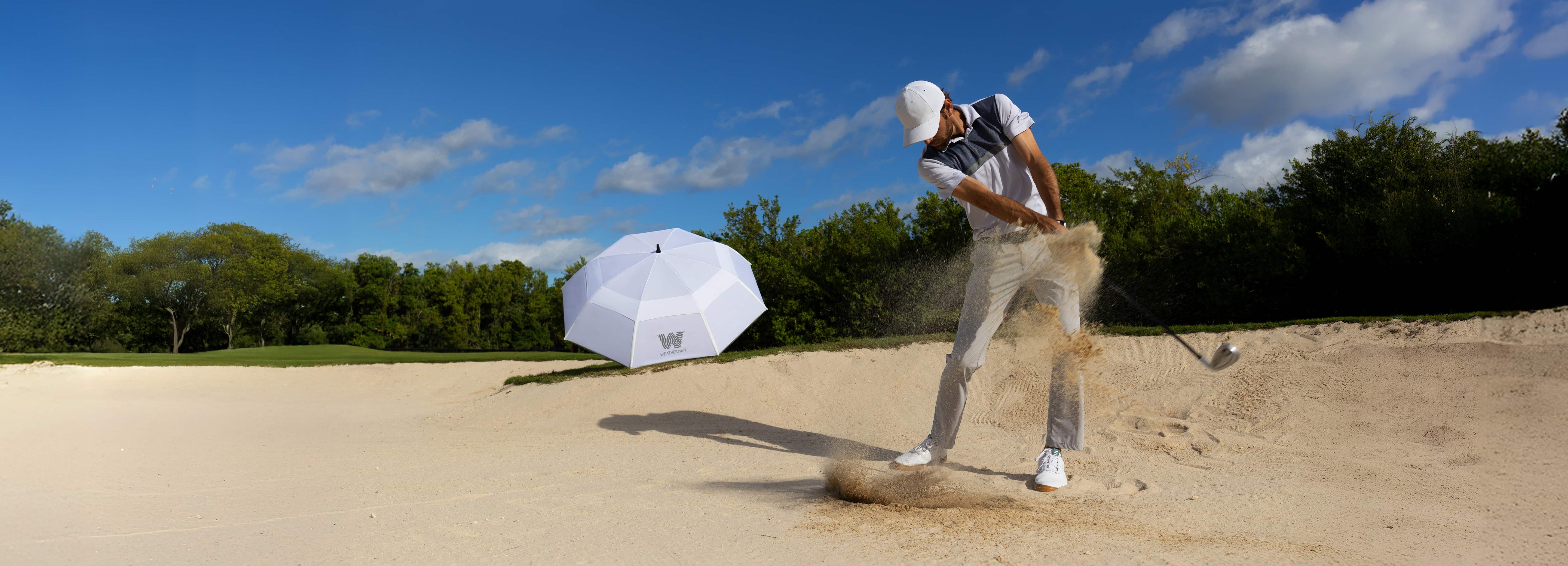 A white Weatherman umbrella stands as a man plays golf