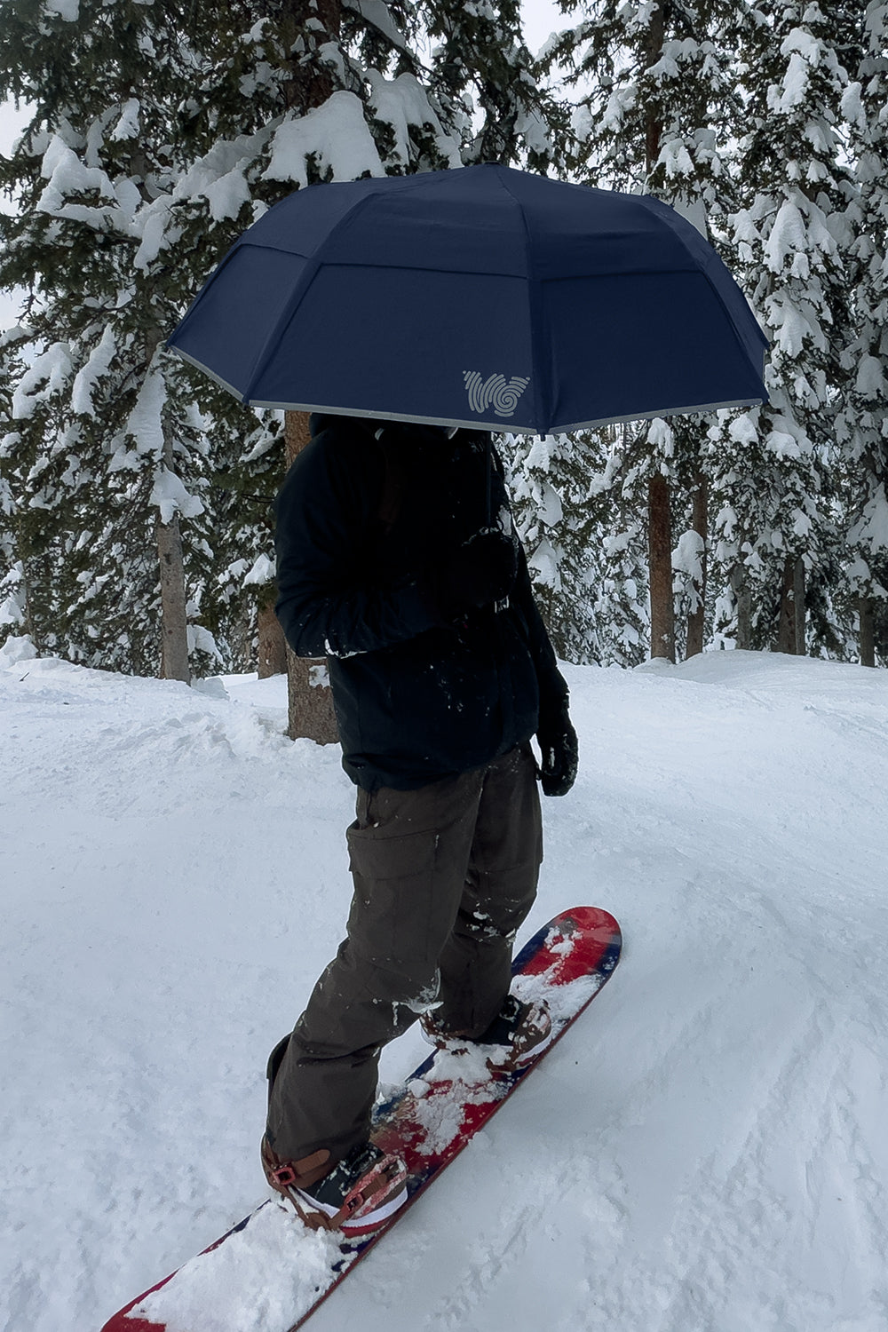 Man snowboarding and holding Weatherman Collapsible Umbrella in navy blue.