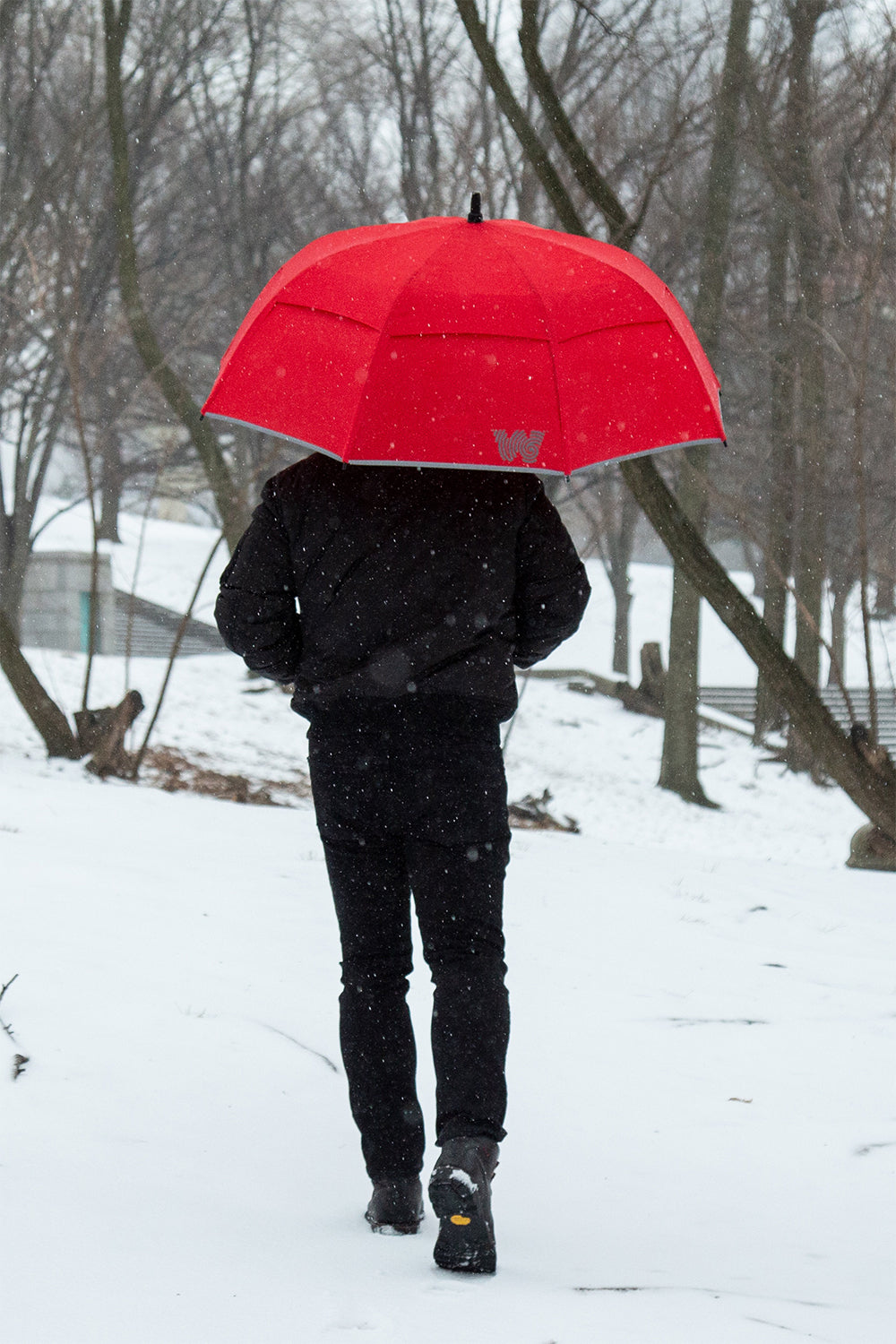 Person walking in the snow with Weatherman Stick Umbrella in red.