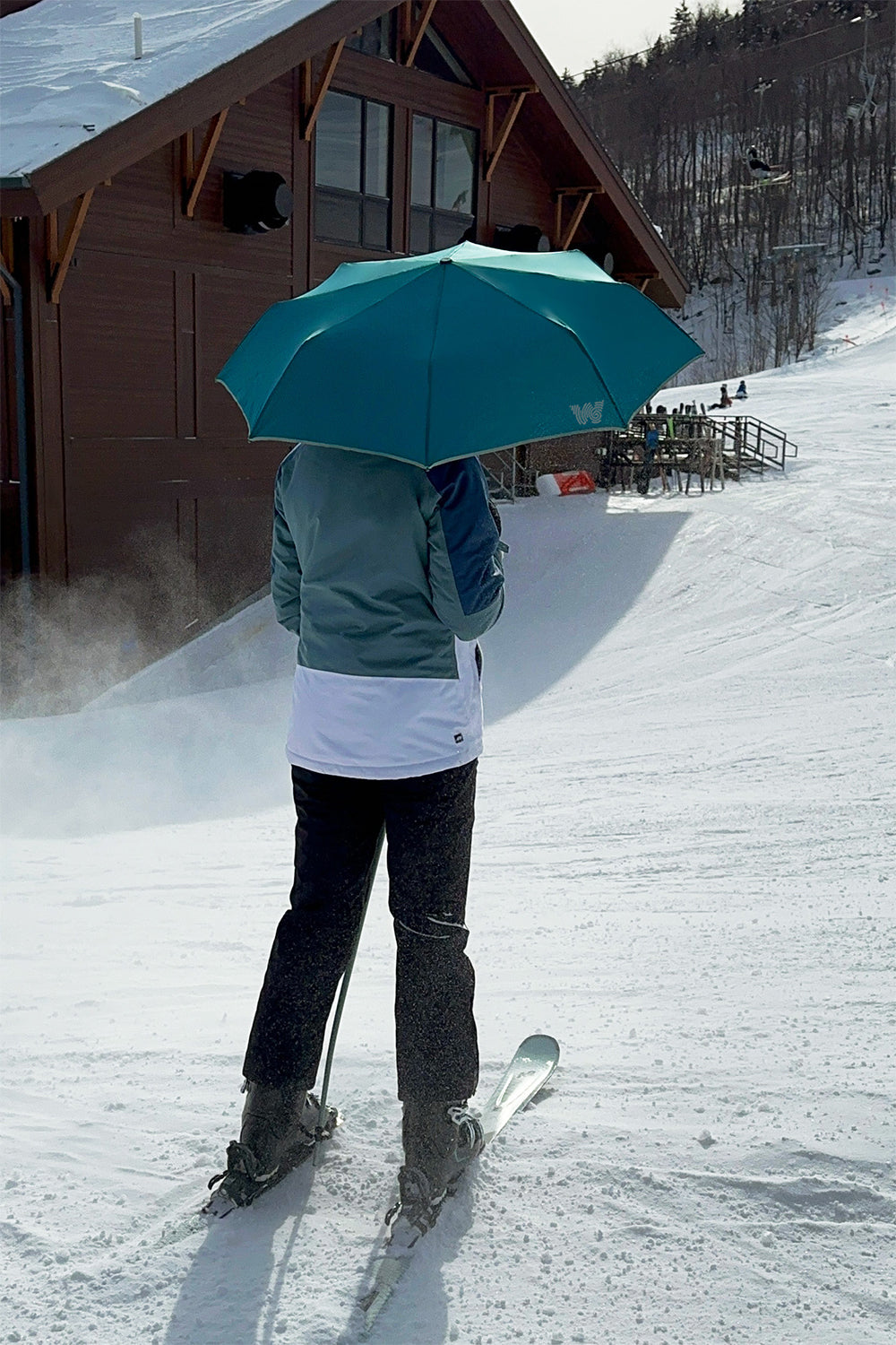 Woman skiing and holding Weatherman Travel Umbrella in deep ocean blue.