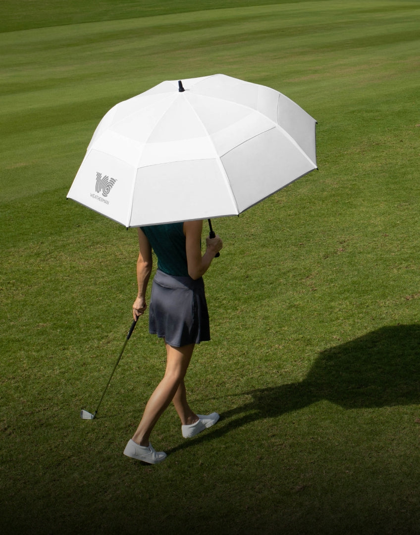 A woman holds a Weatherman umbrella on a golf course