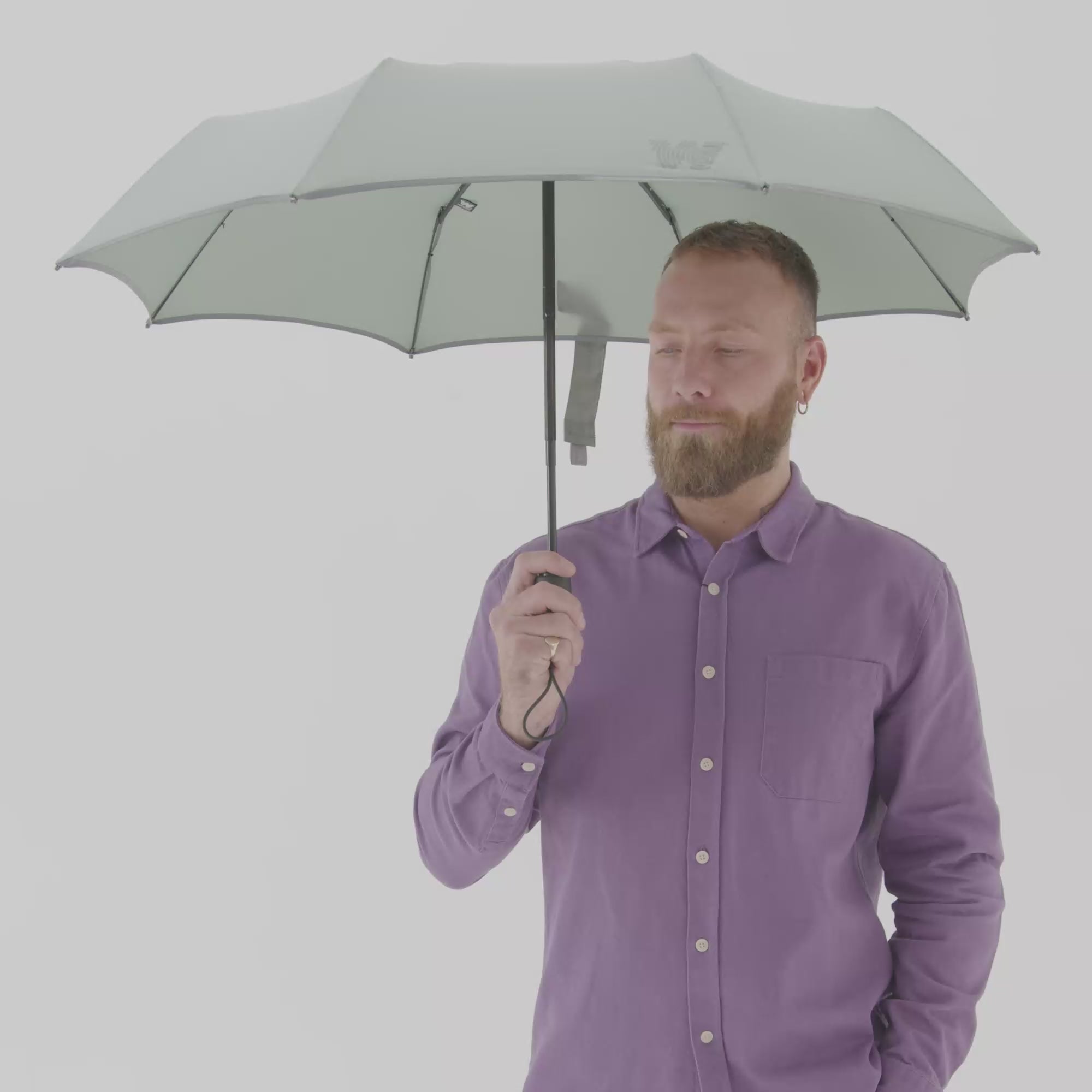 Man closing Weatherman Travel Umbrella in sage green.